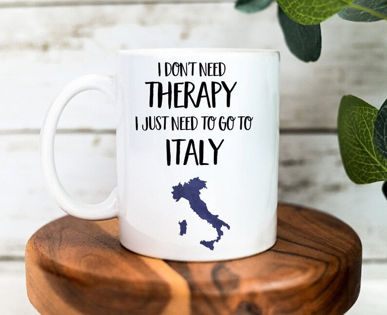 May include: White ceramic mug with a black graphic that reads "I don't need therapy I just need to go to Italy" with a blue outline of Italy.