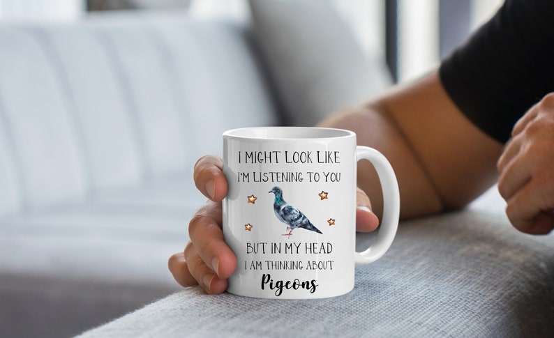 May include: White ceramic coffee mug with a black and white illustration of a pigeon and the text "I might look like I'm listening to you but in my head I am thinking about pigeons".