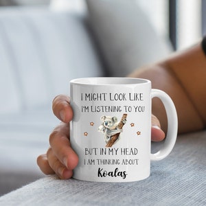 May include: White ceramic coffee mug featuring a koala illustration and the text "I might look like I'm listening to you, but in my head I am thinking about Koalas."