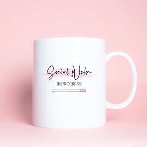 Puede incluir: Taza de cer&aacute;mica blanca con un dise&ntilde;o en negro y rosa que dice "Social Worker In Progress" con una barra de progreso debajo.