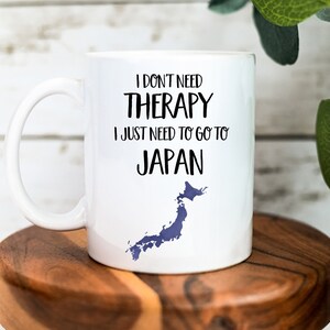 May include: White ceramic mug with a black graphic that reads "I don't need therapy I just need to go to Japan" with a blue outline of the country of Japan.