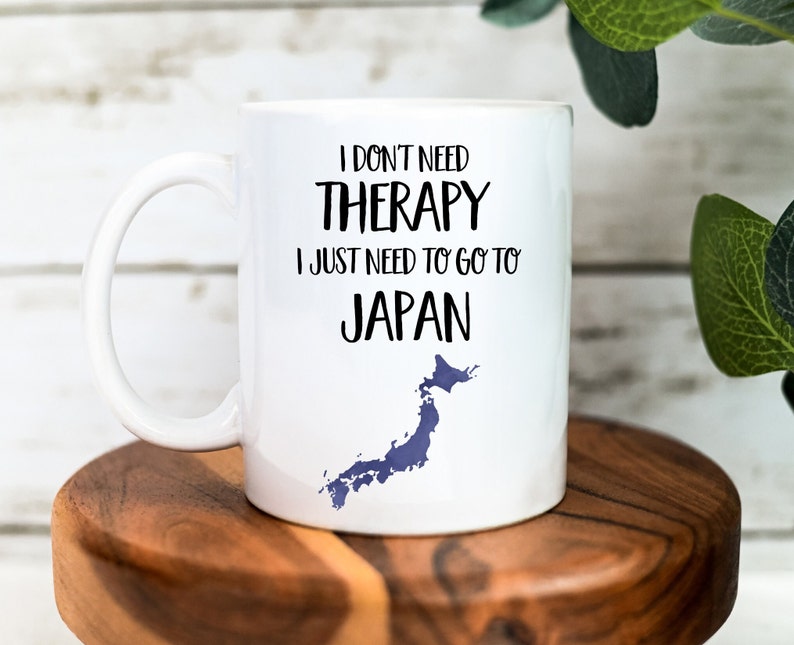 May include: White ceramic mug with a black graphic that reads "I don't need therapy I just need to go to Japan" with a blue outline of the country of Japan.