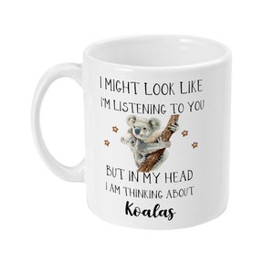 May include: White ceramic mug featuring a black and white illustration of two koalas on a tree branch. The text on the mug reads "I might look like I'm listening to you, but in my head I am thinking about koalas."