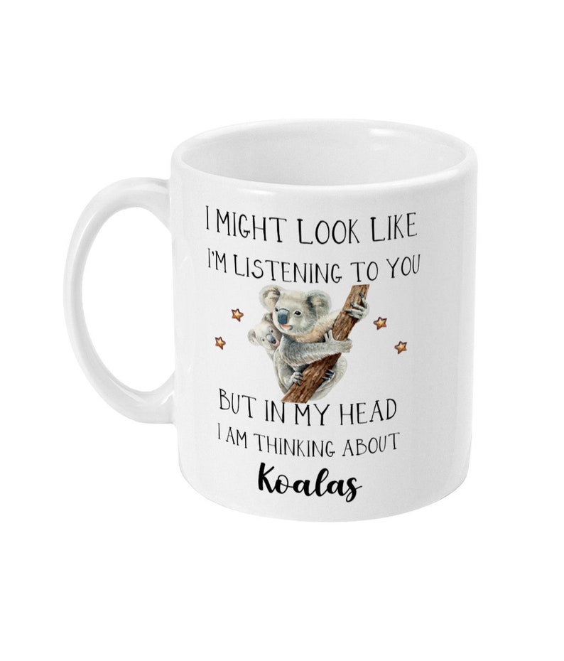 May include: White ceramic mug featuring a black and white illustration of two koalas on a tree branch. The text on the mug reads "I might look like I'm listening to you, but in my head I am thinking about koalas."