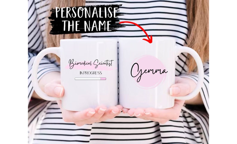 May include: White ceramic mug with a pink circle on the right side that says "Gemma" in black cursive. The left side of the mug has the text "Biomedical Scientist" in black cursive with a pink progress bar underneath that says "In Progress".