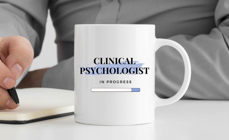 May include: White ceramic mug with a blue and white design. The mug says "Clinical Psychologist" with a progress bar that reads "In Progress".