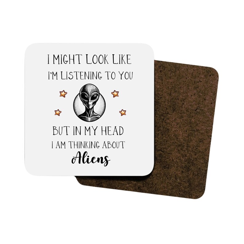 May include: A white coaster with a black and gray alien illustration and the text "I might look like I'm listening to you but in my head I am thinking about Aliens".