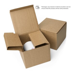 May include: A brown cardboard box with a white mug inside. The box is open and the mug is visible. The box is sitting on a white surface.
