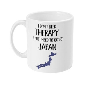 May include: White ceramic mug with a black and white graphic that says "I don't need therapy I just need to go to Japan" with a blue outline of the country of Japan.