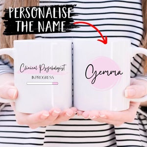 Pu&ograve; includere: Due tazze in ceramica bianca con testo nero. Una tazza dice "Clinical Psychologist In Progress" con una barra di avanzamento rosa. L'altra tazza ha un cerchio rosa con il nome "Gemma" scritto in nero.
