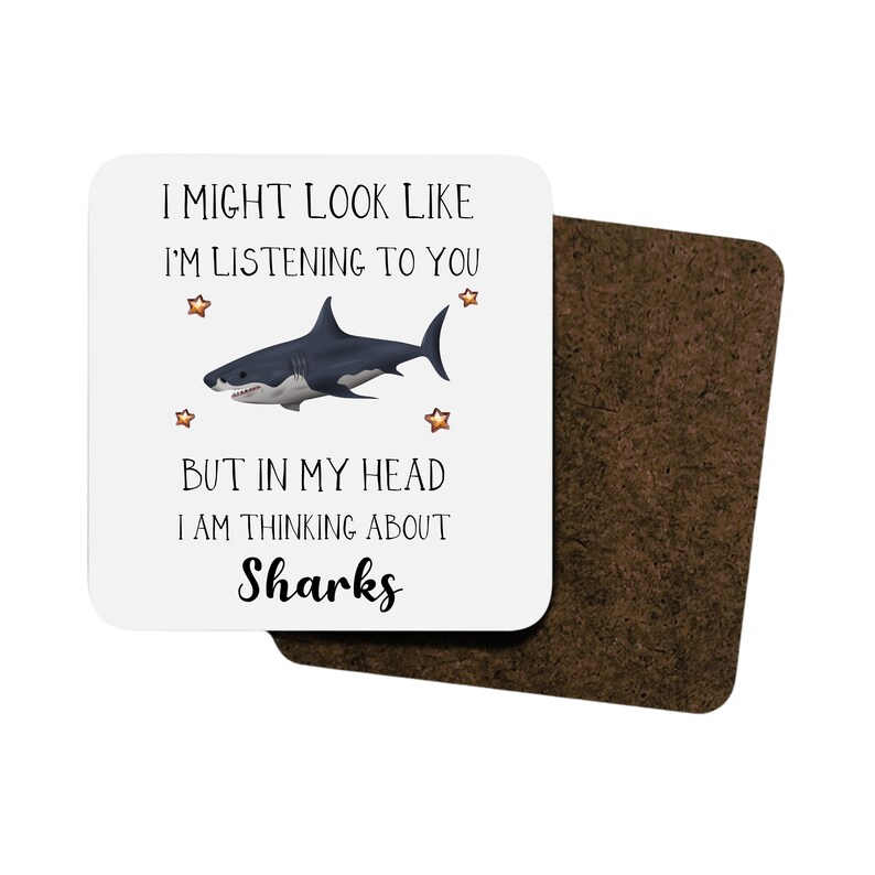 Pu&ograve; includere: Sottobicchiere bianco con un'illustrazione di squalo nero e grigio e il testo "I might look like I'm listening to you but in my head I am thinking about Sharks".