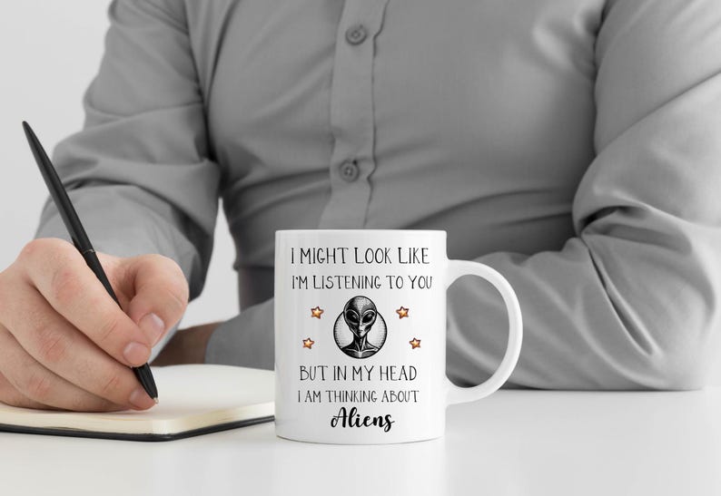 May include: White ceramic mug with a black and white alien graphic and the text "I might look like I'm listening to you, but in my head I am thinking about aliens."