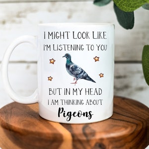 May include: White ceramic mug with a black and gray pigeon illustration. The mug has the text "I might look like I'm listening to you, but in my head I am thinking about pigeons".