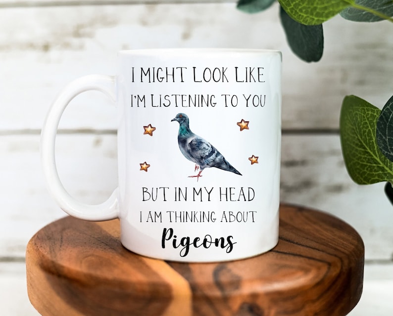 May include: White ceramic mug with a black and gray pigeon illustration. The mug has the text "I might look like I'm listening to you, but in my head I am thinking about pigeons".