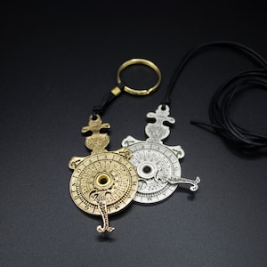 May include: Two antique-style, circular, metal pendants with intricate designs and numbers. The pendant on the left is gold and the pendant on the right is silver. Both pendants are attached to a black cord with a ring.