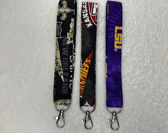 May include: Three colorful fabric keychains with silver metal clasps. The keychains feature the logos of the New Orleans Saints, Kansas City Chiefs, and LSU Tigers.