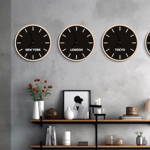 May include: Four round black clocks with white hands and text indicating time zones: New York, London, Tokyo, and Paris. The clocks are mounted on a gray wall above a wooden shelf unit with decorative items.