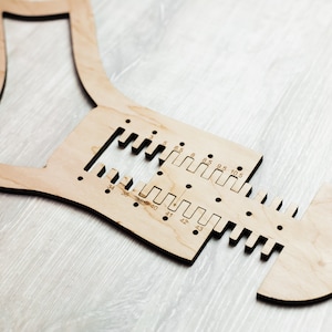 May include: A wooden sock-shaped tool with a ruler and size markings for measuring feet. The tool is made of light brown wood and has a smooth finish.