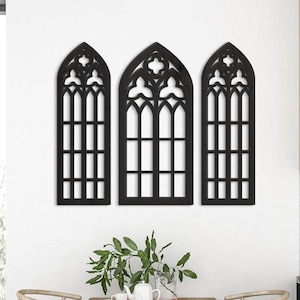 May include: Three black wooden wall decor pieces shaped like arched windows with intricate designs. The windows are arranged in a row, with the middle window slightly larger than the two on either side.
