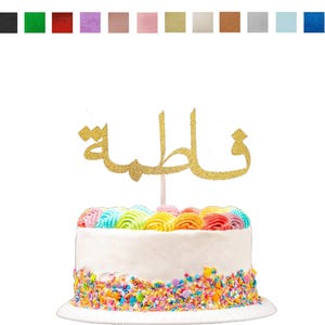 May include: A gold glitter cake topper featuring the Arabic name Fatima in cursive script, displayed on a white cake with colorful frosting swirls and sprinkles, with a row of twelve small colored square swatches shown above the topper.