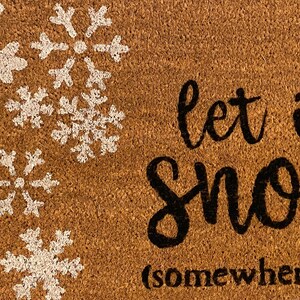 May include: A brown coir doormat with white snowflake designs in the upper left corner. The phrase "let it snow (somewhere else)" is written in black script across the mat, offering a humorous winter welcome.