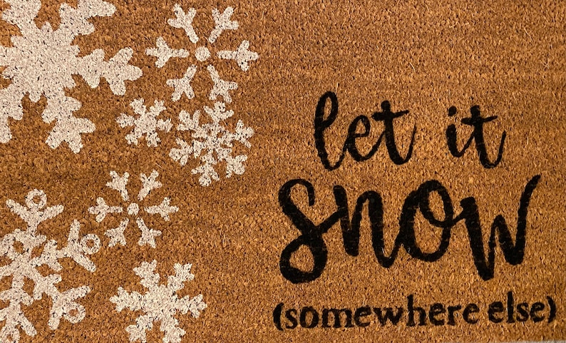 May include: A brown coir doormat with white snowflake designs in the upper left corner. The phrase "let it snow (somewhere else)" is written in black script across the mat, offering a humorous winter welcome.