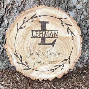 May include: A wooden round slice with a burnt design of a wreath, the letter L, the name Lehman, and the text "David & Caroline June 15, 2022".