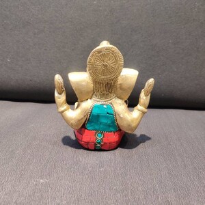 K&ouml;nnte beinhalten: Eine goldfarbene Ganesha-Statue mit roten und gr&uuml;nen Mosaikdetails. Die Statue sitzt mit erhobenen H&auml;nden in einer Geste des Segens.