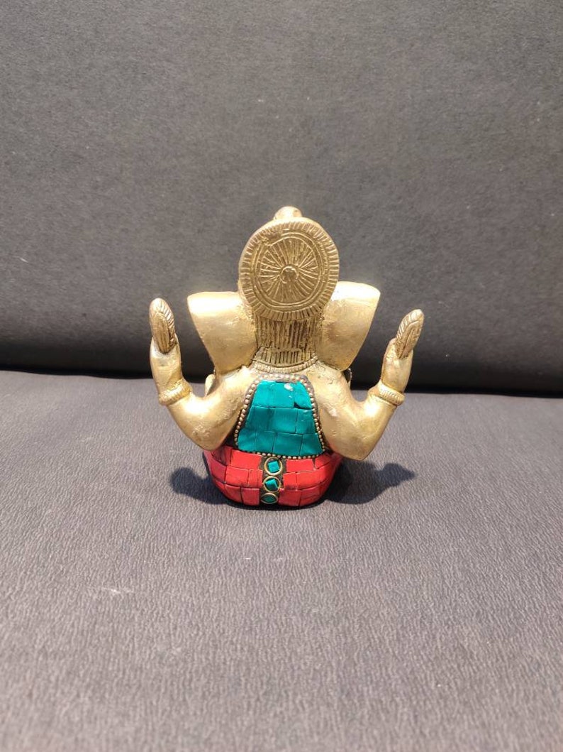 K&ouml;nnte beinhalten: Eine goldfarbene Ganesha-Statue mit roten und gr&uuml;nen Mosaikdetails. Die Statue sitzt mit erhobenen H&auml;nden in einer Geste des Segens.