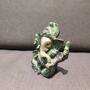 K&ouml;nnte beinhalten: Eine kleine, gr&uuml;ne und goldene Ganesha-Statue mit einem detaillierten Design. Die Statue sitzt mit gekreuzten Beinen und erhobenem R&uuml;ssel.