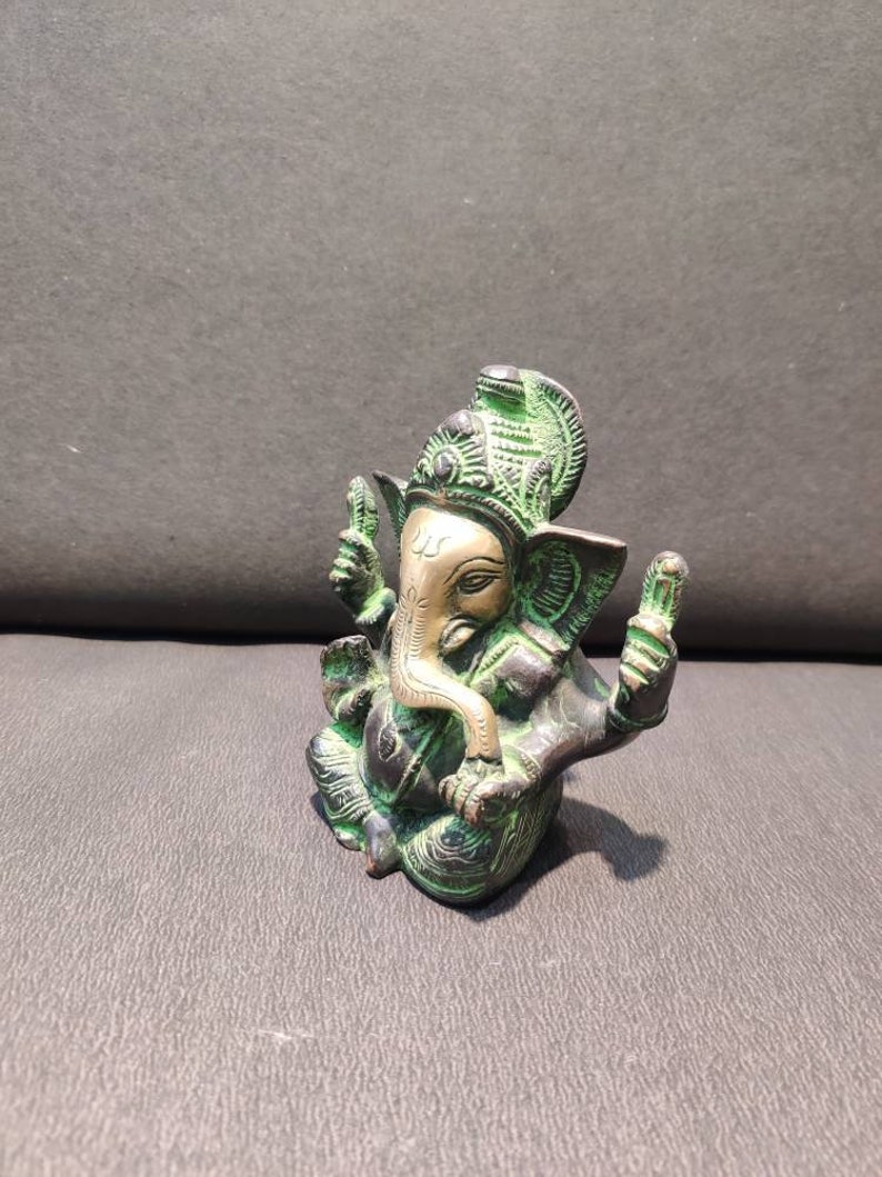 K&ouml;nnte beinhalten: Eine kleine, gr&uuml;ne und goldene Ganesha-Statue mit einem detaillierten Design. Die Statue sitzt mit gekreuzten Beinen und erhobenem R&uuml;ssel.