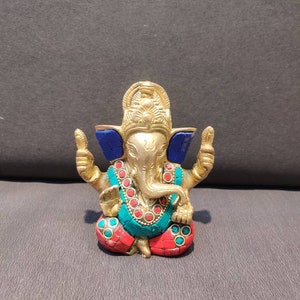 K&ouml;nnte beinhalten: Eine goldfarbene Ganesha-Statue mit blauen, roten und gr&uuml;nen Akzenten. Die Statue sitzt mit erhobenen H&auml;nden in einer Segensgeste.