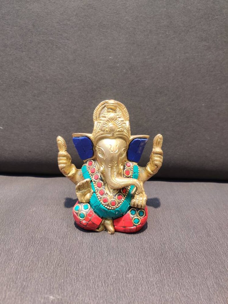 K&ouml;nnte beinhalten: Eine goldfarbene Ganesha-Statue mit blauen, roten und gr&uuml;nen Akzenten. Die Statue sitzt mit erhobenen H&auml;nden in einer Segensgeste.