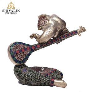Könnte beinhalten: Eine silberfarbene Elefantenskulptur, die Sitar spielt. Sitar und Sockel sind mit roten, blauen und grünen Mosaikeinlagen verziert. Die Skulptur stammt von Shivalik Emporium.