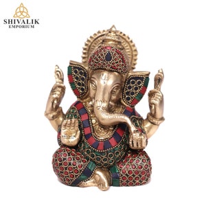 Könnte beinhalten: Eine goldfarbene Messingstatue von Ganesha, dem hinduistischen Gott der Weisheit und des Wohlstands. Die Statue ist mit roten, grünen und blauen Edelsteinen verziert und hat ein detailliertes Design. Die Statue sitzt in meditativer Haltung mit dem Rüssel nach oben gerollt.