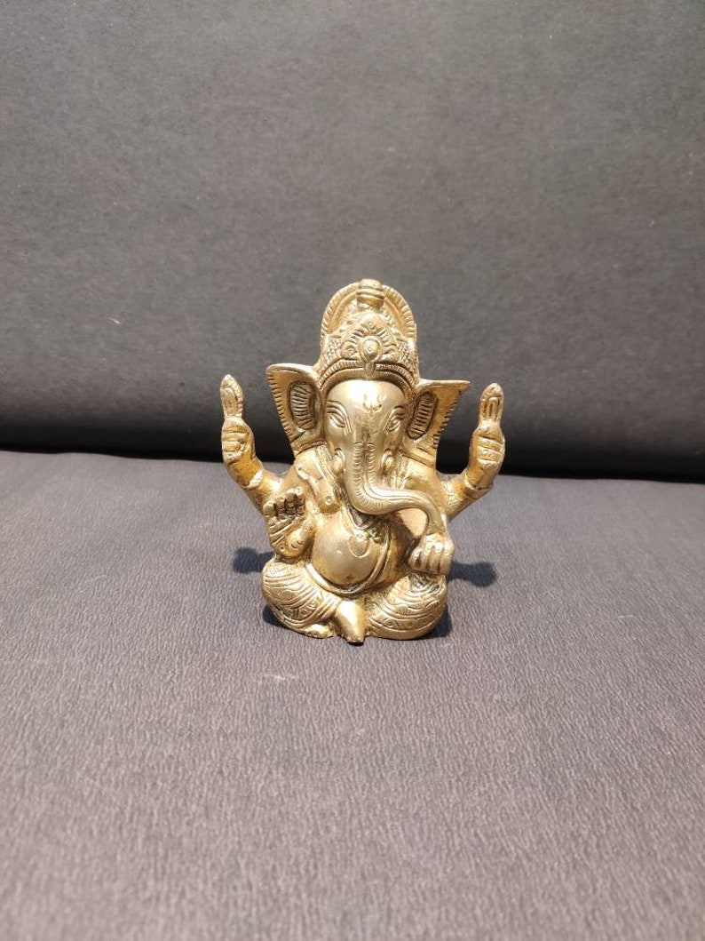 K&ouml;nnte beinhalten: Eine goldfarbene Metallstatue von Ganesha, dem hinduistischen Gott der Weisheit und des Wohlstands. Die Statue ist aufwendig detailliert und zeigt Ganesha sitzend mit erhobenem R&uuml;ssel und seinen H&auml;nden in einer Segensgeste.