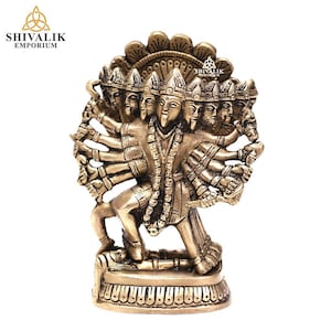 Puede incluir: Una estatua de metal dorado de una deidad hindú con ocho brazos y múltiples cabezas. La deidad está de pie sobre una base con un diseño decorativo. La estatua es un artefacto religioso tradicional.