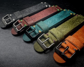 May include: A collection of colorful leather watch straps in various shades, including black, brown, teal, olive green, and orange. Each strap features a metal buckle and contrasting stitching. The straps are arranged in a row, showcasing their different colors and textures.