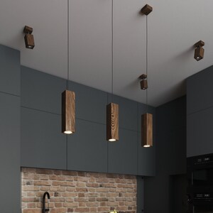 Peut inclure: Une cuisine moderne avec un plan de travail en bois et un dosseret en brique. Trois lampes suspendues en bois pendent au-dessus du plan de travail, et un bol d'oranges se trouve sur le comptoir.