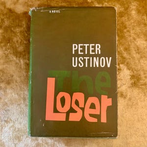 May include: A vintage hardcover book titled "The Loser" by Peter Ustinov. The cover is dark green with the title in large orange letters and the author's name in white. The words "A Novel" are at the top.