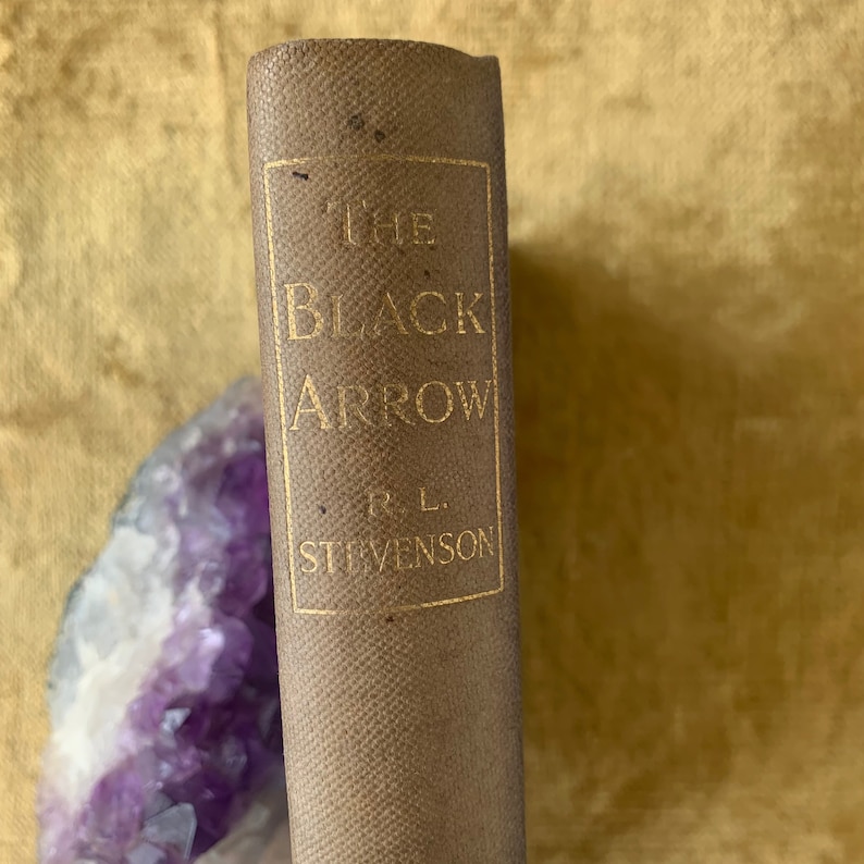 May include: A brown leather-bound book with gold lettering on the spine. The title is "The Black Arrow" by R.L. Stevenson.