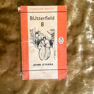 Puede incluir: Una portada de libro de bolsillo vintage de Penguin Books con fondo naranja. El título es "Butterfield 8" de John O'Hara. La portada presenta una ilustración en blanco y negro de una mujer caminando por una calle de la ciudad.