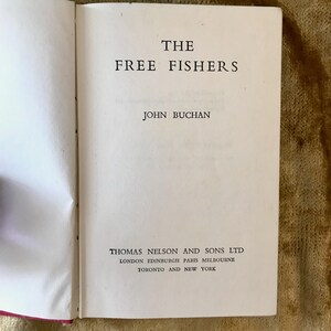 Può includere: La copertina di un libro intitolato "The Free Fishers" di John Buchan. Il libro è pubblicato da Thomas Nelson and Sons Ltd. e stampato a Londra, Edimburgo, Parigi, Melbourne, Toronto e New York.