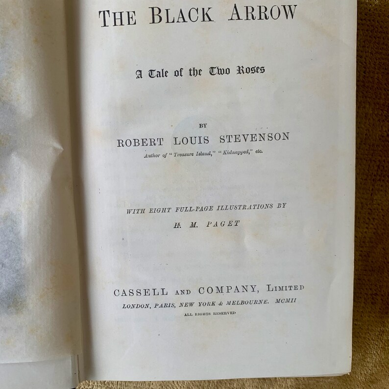May include: The Black Arrow, a Tale of the Two Roses, by Robert Louis Stevenson, author of Treasure Island and Kidnapped. The book cover features the title in a black font with a decorative arrow design. The author's name is in a smaller font below the title. The book was published by Cassell and Company, Limited in 1911.