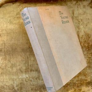 Könnte beinhalten: Ein Vintage-Hardcover-Buch mit dem Titel "The Young Rider" mit dem Aufdruck "COUNTRY LIFE." auf dem Rücken.