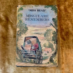 May include: A hardcover book titled Miss Clare Remembers by Miss Read. The cover features a watercolor illustration of a horse-drawn cart loaded with items, traveling along a dirt path through a landscape with green trees and a small house.