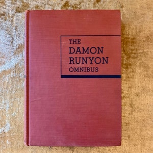 May include: A red hardback book with the title "The Damon Runyon Omnibus" printed in black on the front cover.