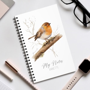 Könnte beinhalten: Ein weißes Spiralnotizbuch mit einer Aquarellillustration eines Rotkehlchens auf einem Ast. Das Notizbuch hat den Text "My Notes ANNETTE" in eleganter Schrift.