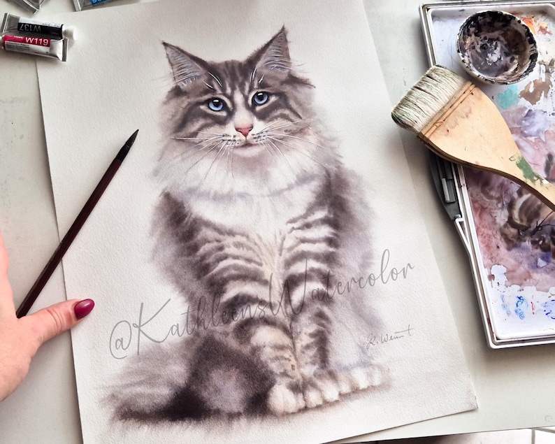 May include: A watercolor painting of a long-haired grey and white tabby cat with striking blue eyes. The cat is depicted in a seated position, facing forward. The artwork features the cursive text @KathleensWatercolor and a signature in the corner.