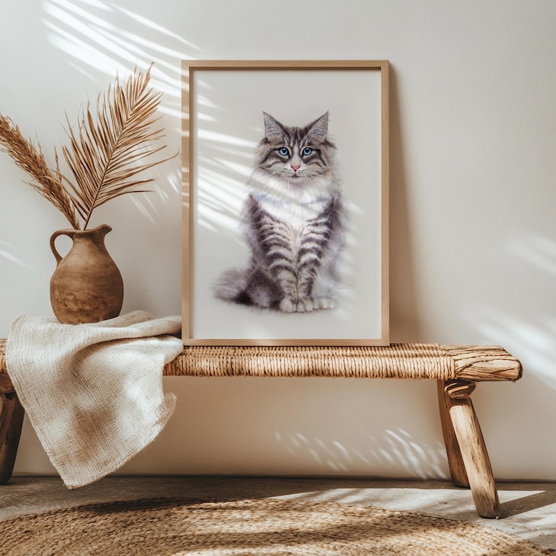 May include: A framed wall art print featuring a portrait of a fluffy grey and white tabby cat with striking blue eyes. The cat is depicted in a seated position, facing forward, with detailed fur textures and a clear, focused gaze on a light background.